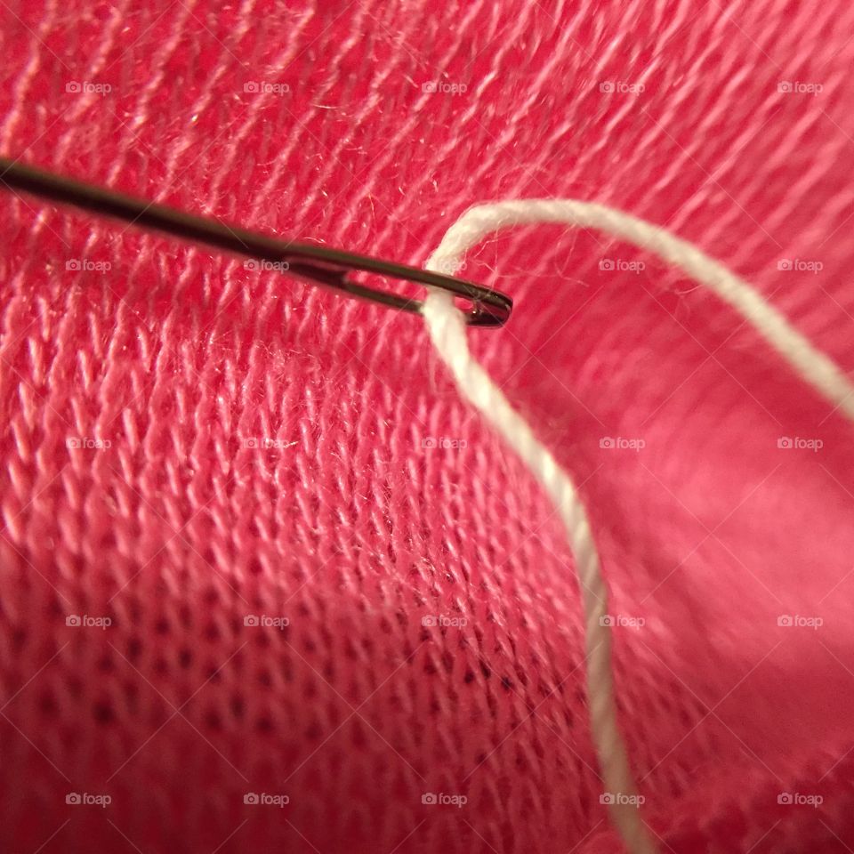 A macro view of a sewing needle pulling white thread through pink knit fabric.