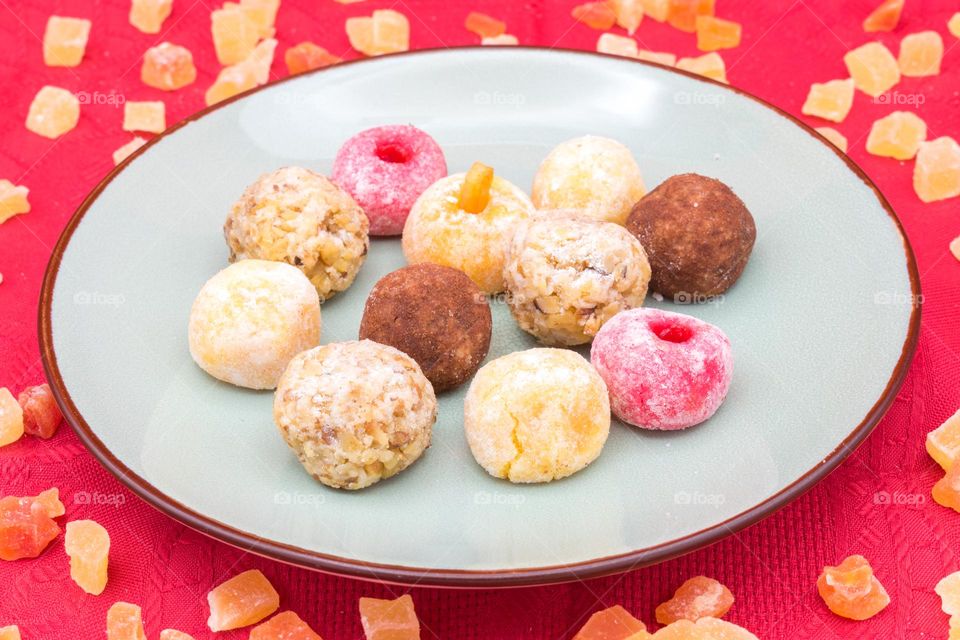 Plate with panellets (traditional sweet for All Saints' Day in Catalonia, the Balearic Islands, Levante and Aragón) set on a red tablecloth and surrounded by cubes of dried fruit.