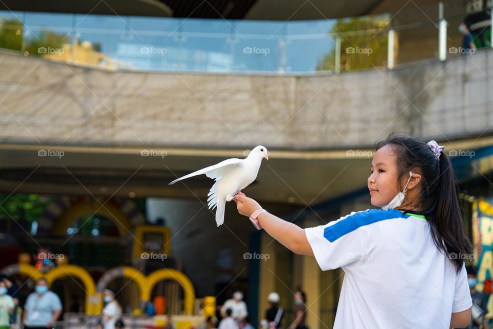 The pigeon is sitting on the hand of a kid.