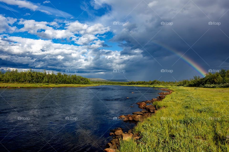 Clean clear river in Lapland in Sweden with a rainbow on the background.