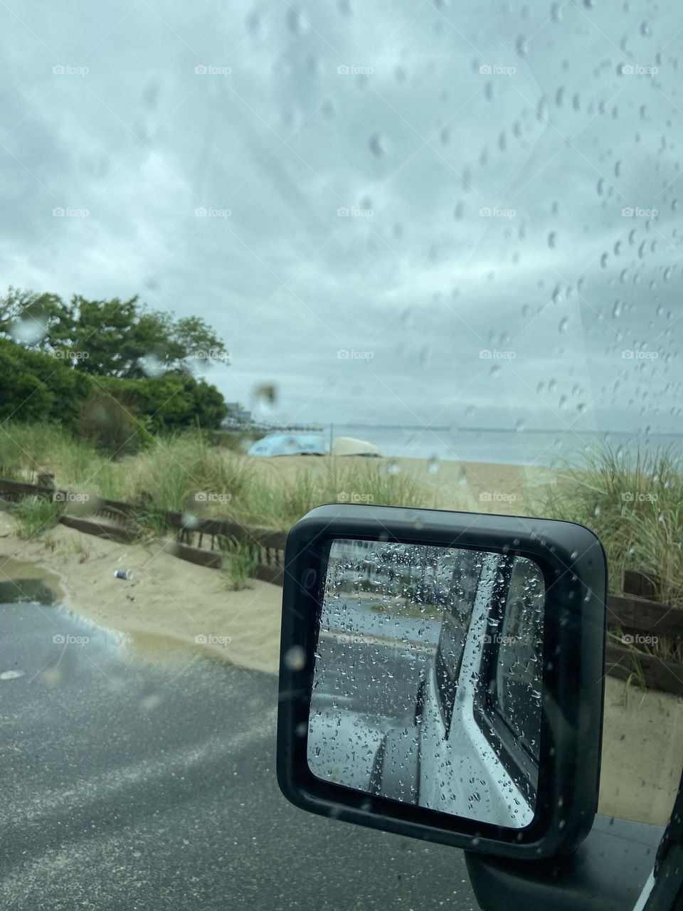 Sitting by the water in the rain at a small park and playground in Lavallette, NJ. This photo was taken from my Jeep through the driver’s side window. Rain drops are scattered on the window and the mirror, and the sky is turning gray above the bay. 