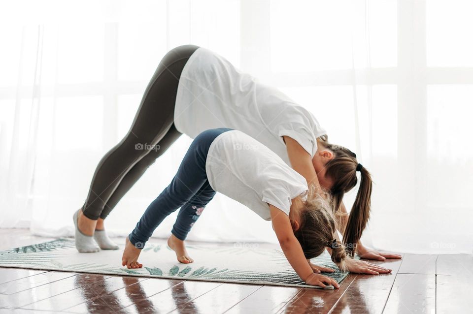 Happy mom and little daughter doing morning yoga together at bright interior home