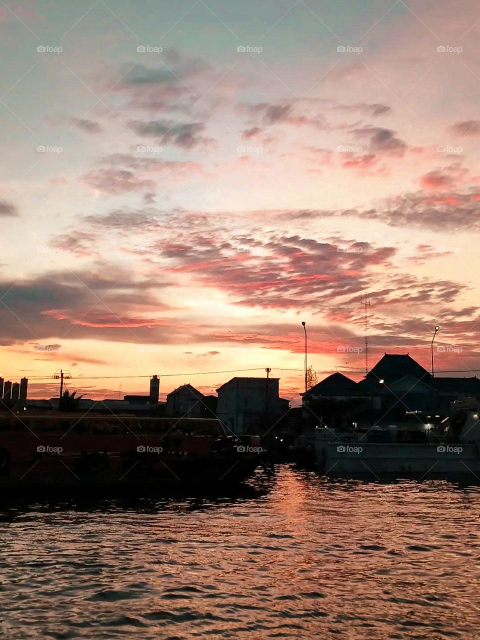 Portrait of a beautiful sunset in the harbor, with the sky colored pink and orange, and buildings and ships visible as silhouettes