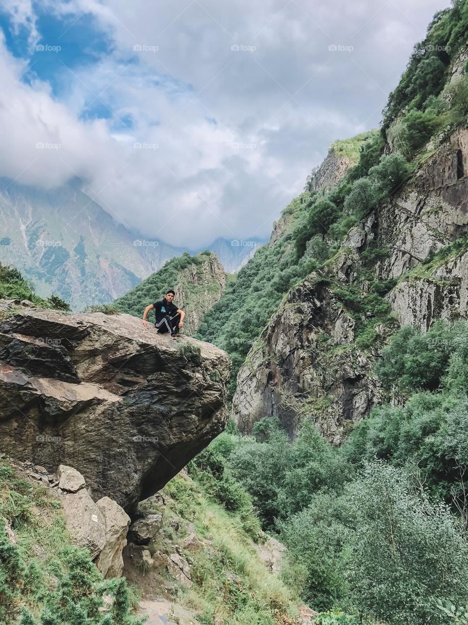 Young man sitting on the rock edge enjoying mountain landscape