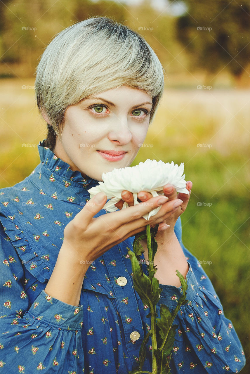 Big portrait of beautiful young smiling woman with short hear and with white flower in her hands.