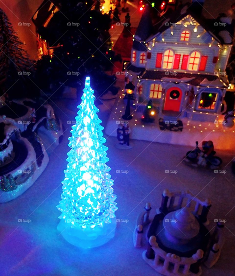 A glowing Christmas tree in the town square of a decorative Christmas village display. 