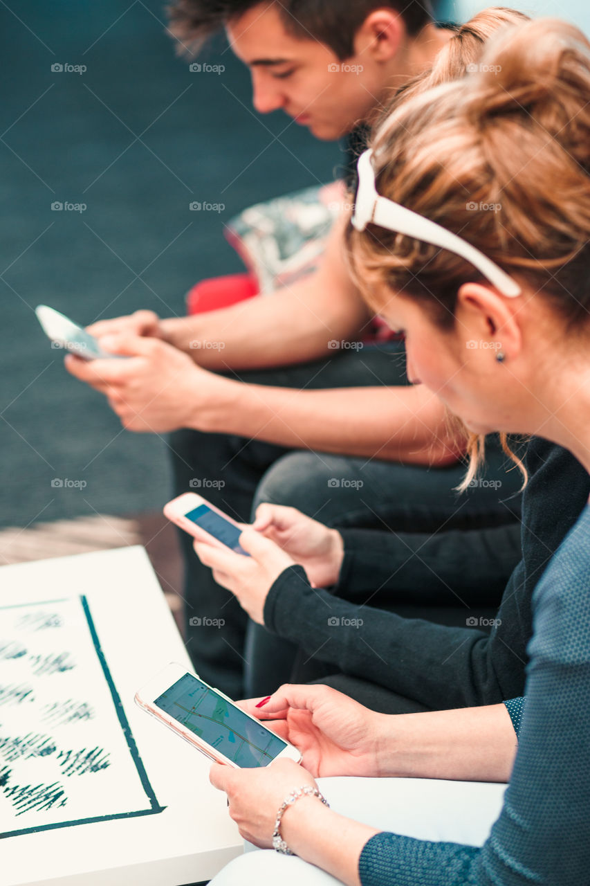 Family members using mobile phones together, sitting on sofa in lounge in hotel