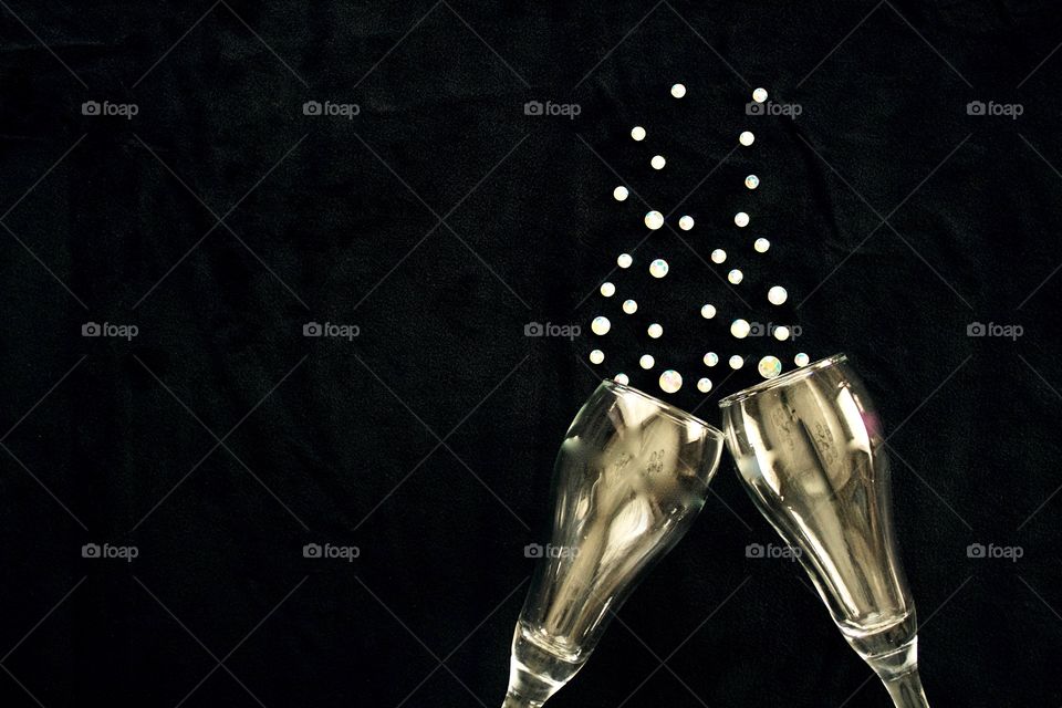 Flat lay of gold-tinted champagne glasses and  rhinestone bubbles on black background