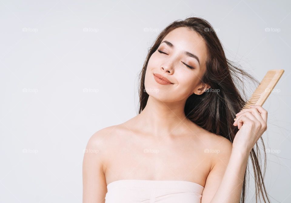 Beauty portrait of happy smiling asian woman with dark long hair combing wooden comb on white background isolated