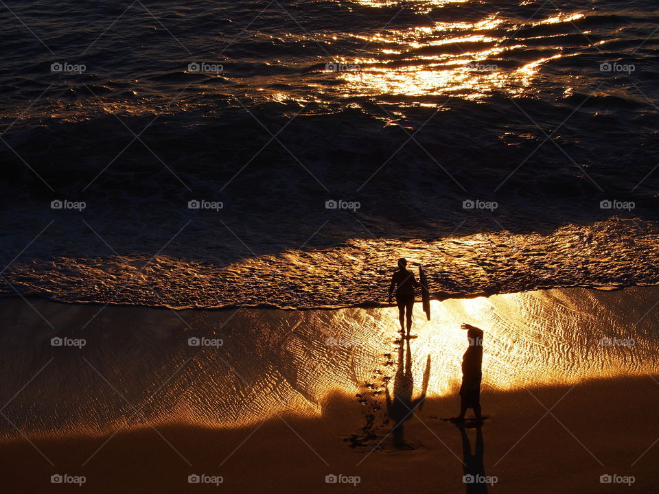 Silhouette of two people standing on the shore at sunset