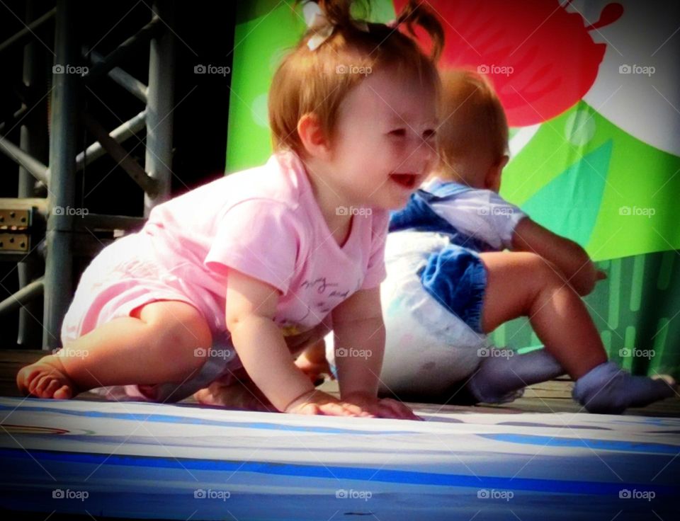 Happiness. The smile of a child. A little girl sits on the podium with a sincere smile. The girl has two funny ponytails on her head. Photo from which the beholder has a smile on his face and happy emotions