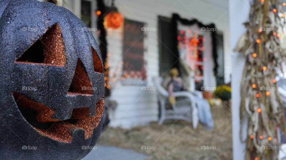 A pumpkin that has been two toned dipped in alternate glitter colors. A country porch, viewed through a soft bokeh serves as the background.