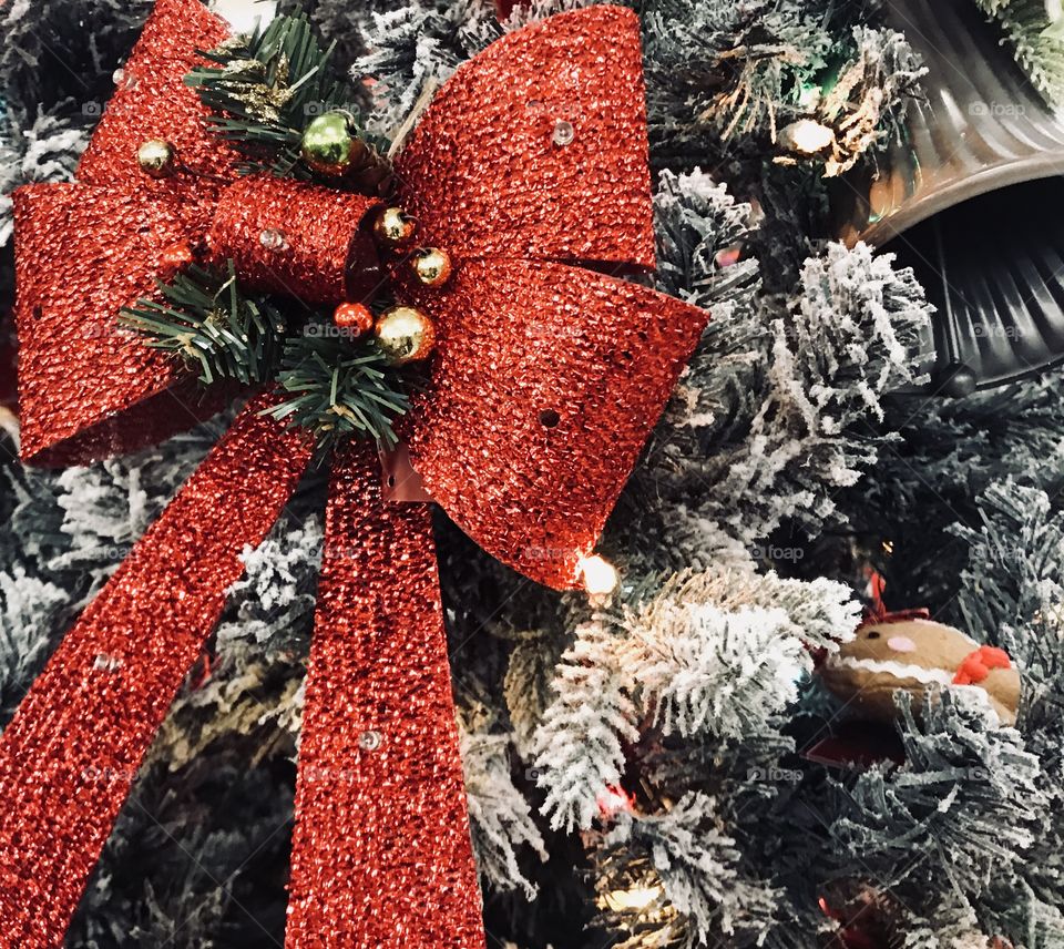 A beautiful bright red ribbon on the Christmas tree surrounded by shining colorful Christmas lights and a gold and silver bell.