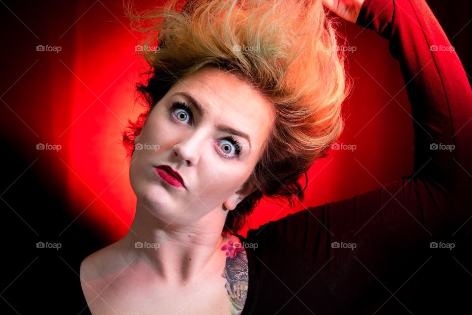 Crazy Daisy . A young woman with bulging eyes and zombie makeup pulls her hair and stares at the camera, red background. 