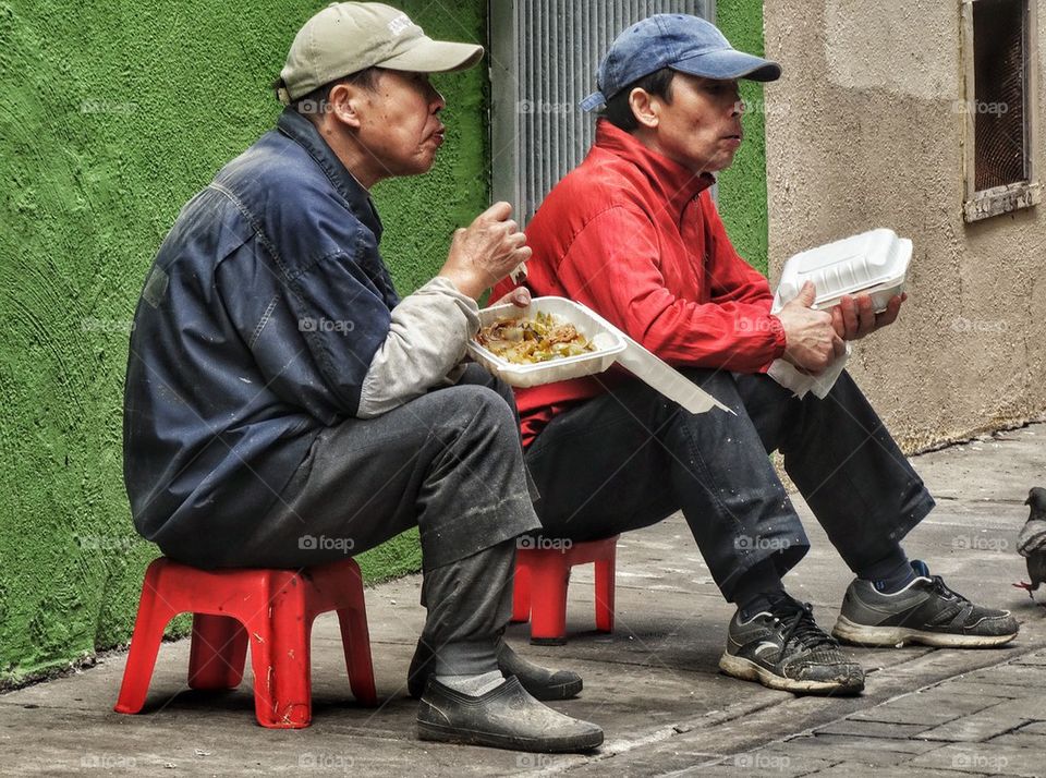 Pair Of Workers Eating Lunch In Chinatown. Workers Taking A Lunch Break In A Back Alley
