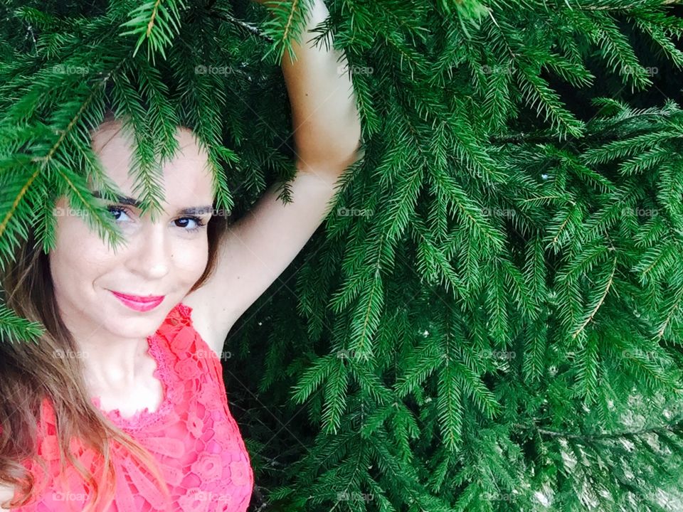 Portrait of woman with red lips surrounded by pine cone trees