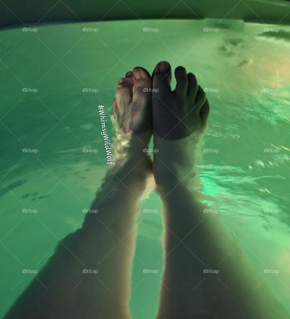 Feet submerged in the clear water of a hot tub. Lit with a soft, yellow light.