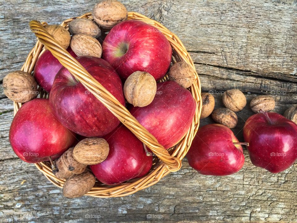 Wooden basket full of red apples and nuts with red apples and nuts beside 