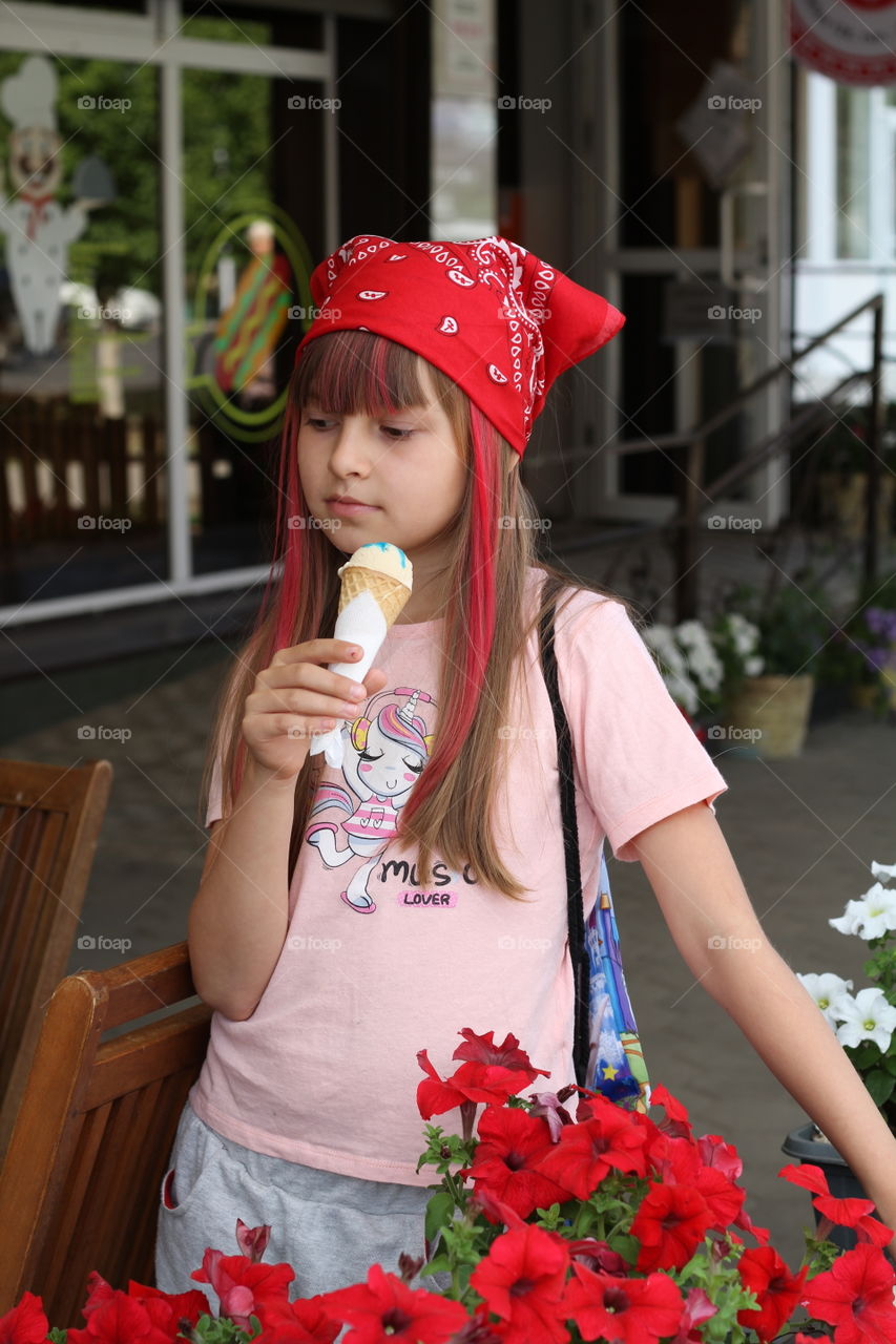 девочка в красной бандане ест мороженое , в летнем кафе