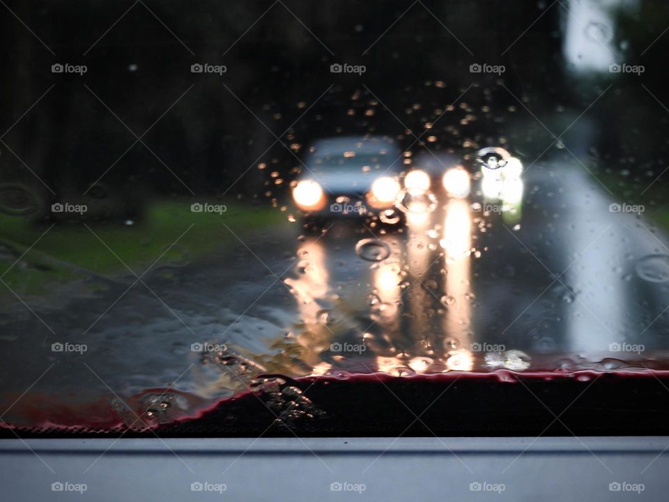 Commuting: cars driving on the opposite direction from the pickup truck driving while it’s raining with the lights on.