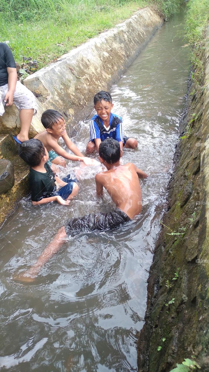A small child who is cool playing in a small river on the edge of a rice field