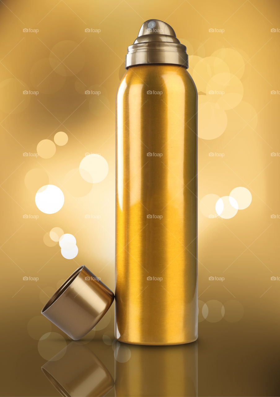 Gold colored deodorant can on golden blurred bokeh background