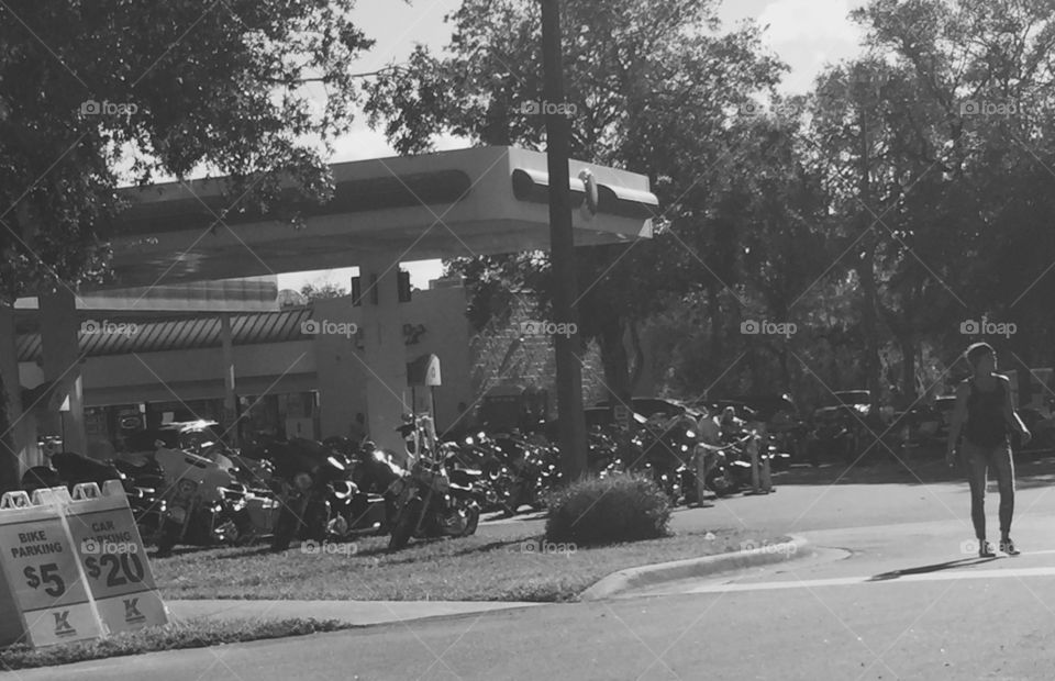 Motorcyclists in Daytona Beach and Ormond Beach Florida during Biketoberfest biker festival. Rear view with men and women riding Harley Davidson, Honda, BMW motorbikes, trikes and 3-wheelers. Biker parking at gas station. Monochrome black and white with pedestrian.