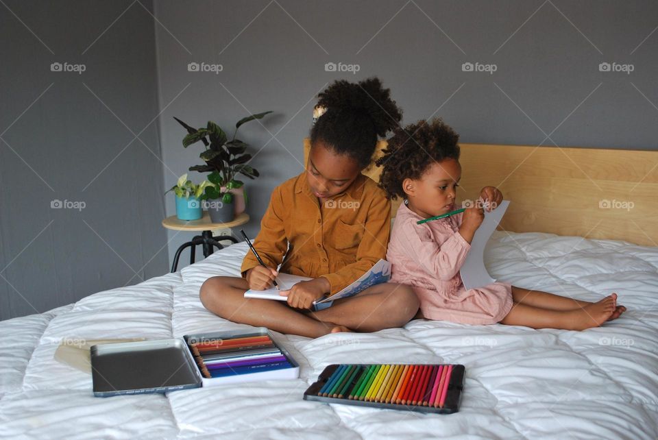 Little girls of mixed race coloring on the bed