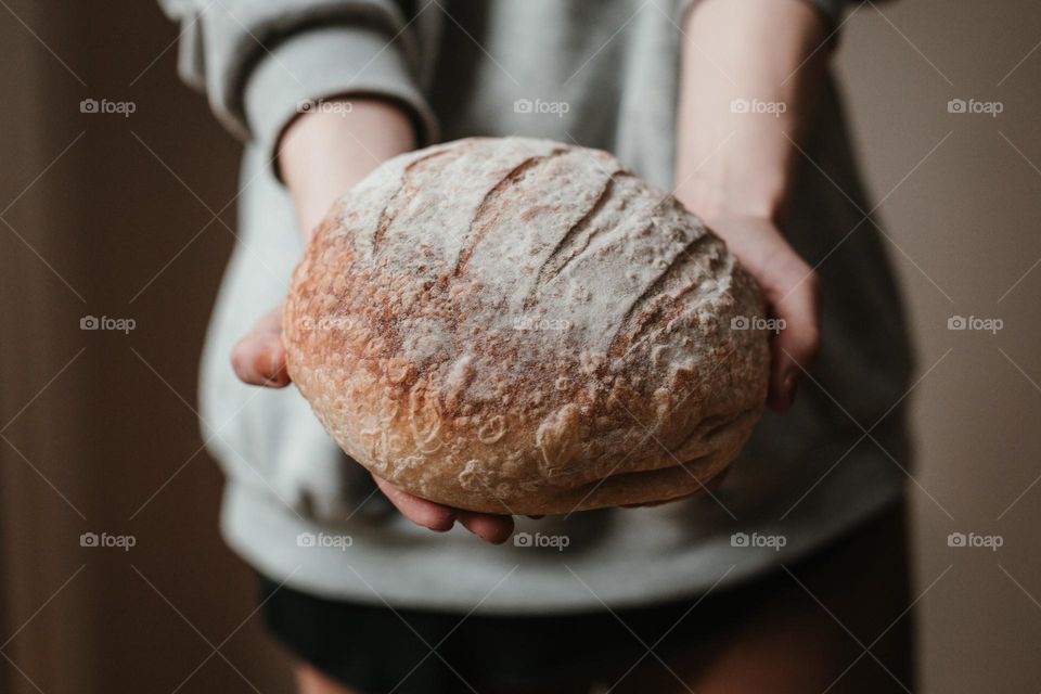 Hold the freshly baked sourdough bread with both hands and lightly dust it with flour.