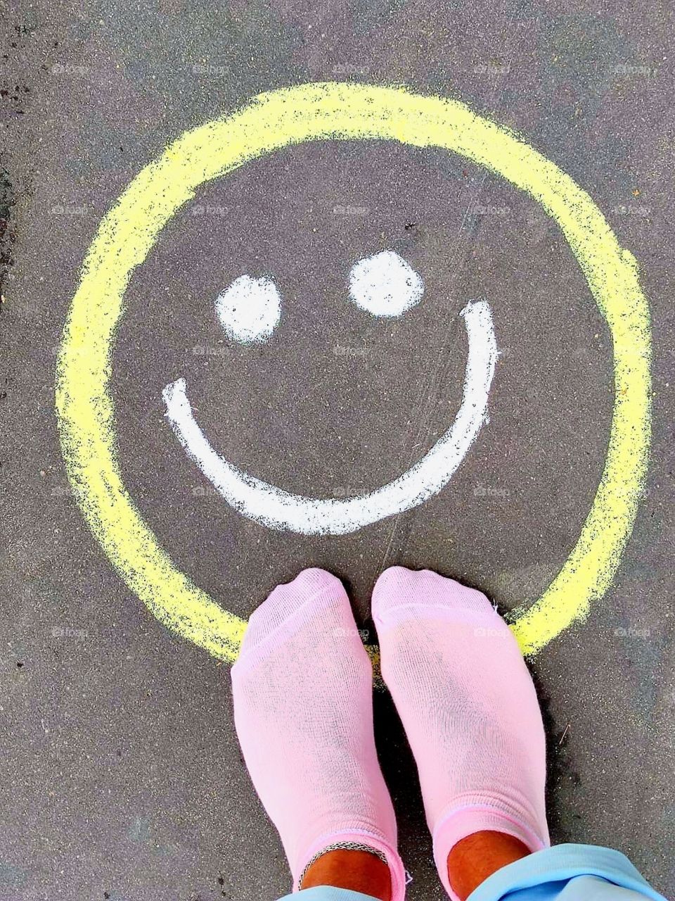 On the gray asphalt yellow smiley, which smiles. Feet in pink socks stand next to emoticons