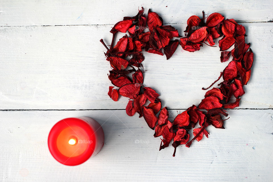 Heart of rose petals and red candle on a white background