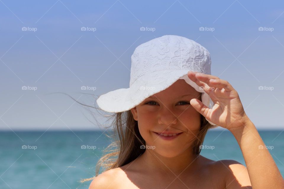 Portrait of smiling beautiful girl of 7-8 years in white sun hat looking at camera