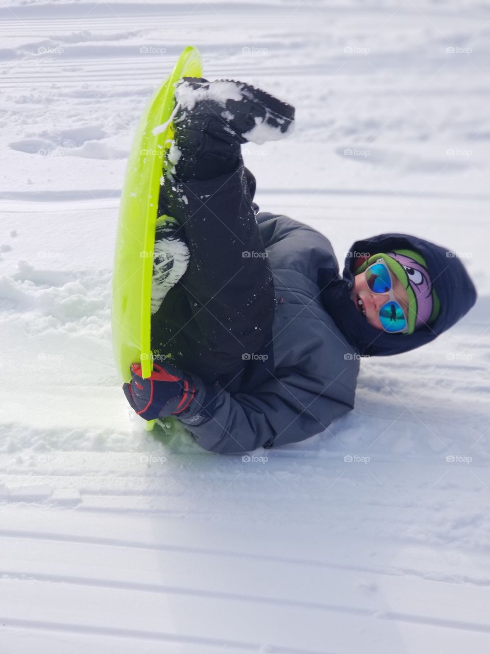 Young boy tipped over on a sled in the snow outdoors during winter