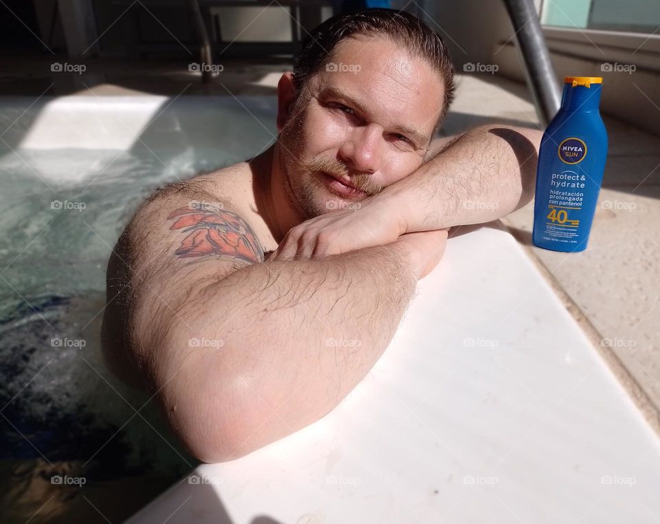 hombre  rubio en yacuzzi al sol con Nivea sun Protec & hidrat con tatuajes