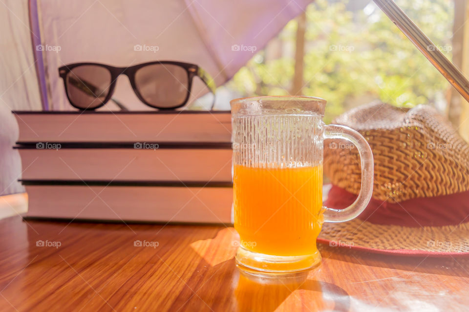 Super Protection from the sun. Sunburn risk concept. Umbrella protecting beautiful woman things. Books, sunglasses, orange juice and a straw hat. Summer holiday concept with copy space room for text.
