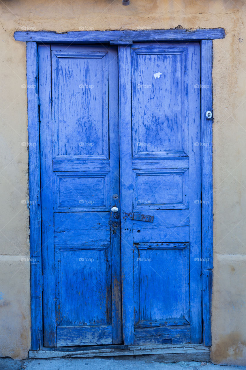 Purple blue wooden double doors on a grey wall. New paint on worn doors. One of the doors is slightly open