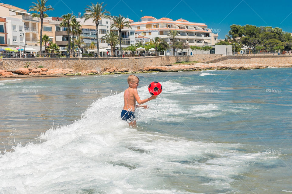 Boy is playing with red ball in seashore