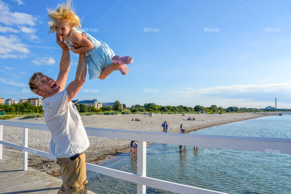 A father carrying her daughter while standing on the pier