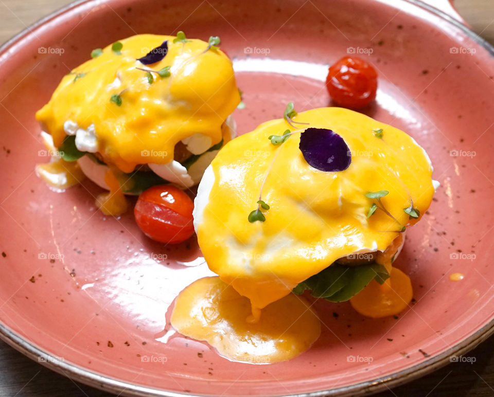 Eggs Benedict. Toasted English muffins, salmon, poached eggs, buttery hollandaise sauce and tomatoes. Homemade Classic Egg Benedict with fried salmon, served in a clay frying pan, flower petal on top.