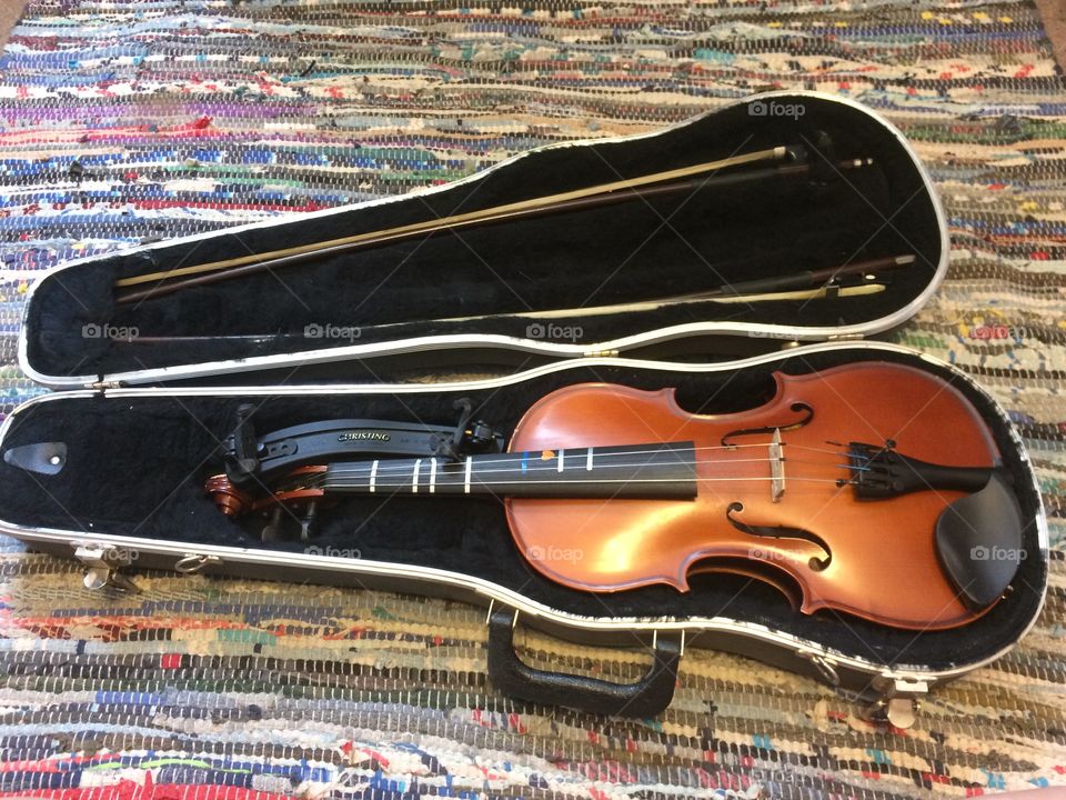 Violin and bow in case on colorful rug. 