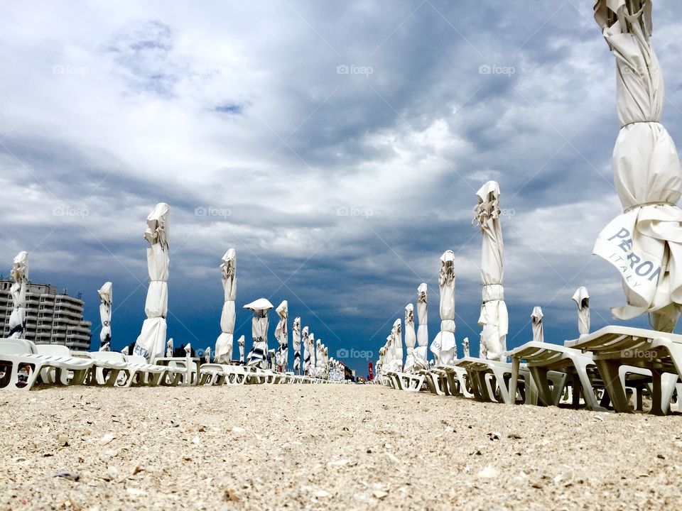 Empty beach with sunbeds and umbrellas and stormy clouds above