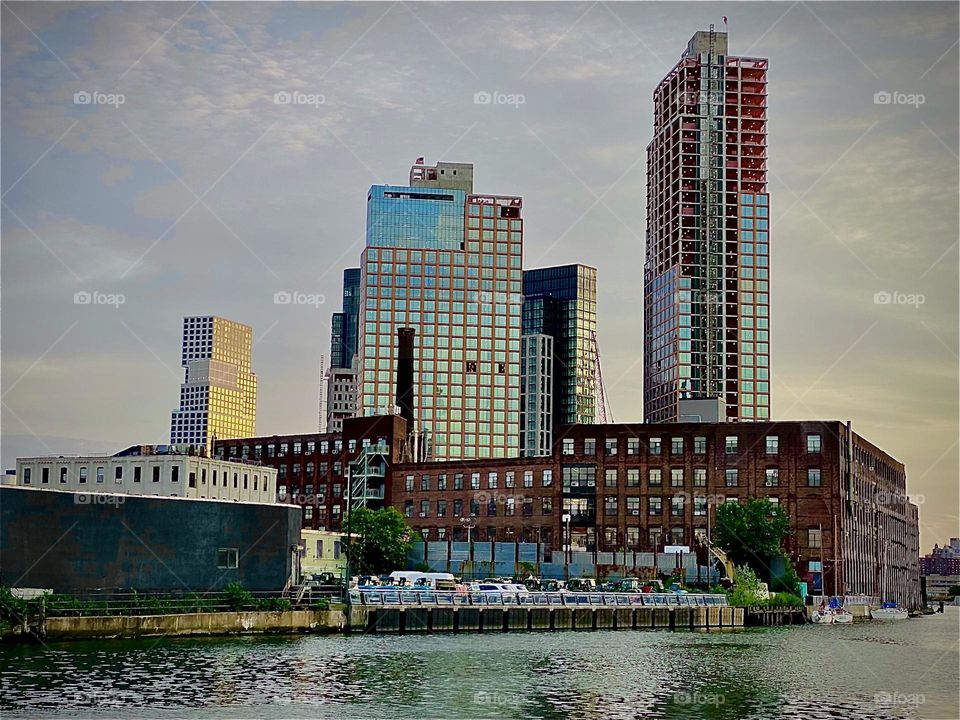 The buildings on the “Greenpoint”, Bklyn side of the “Pulaski Bridge” at “Newtown Creek” can be seen from the parking lot by the wall we climb regularly to venture out to the boat. 2022. Hypnotic Productions