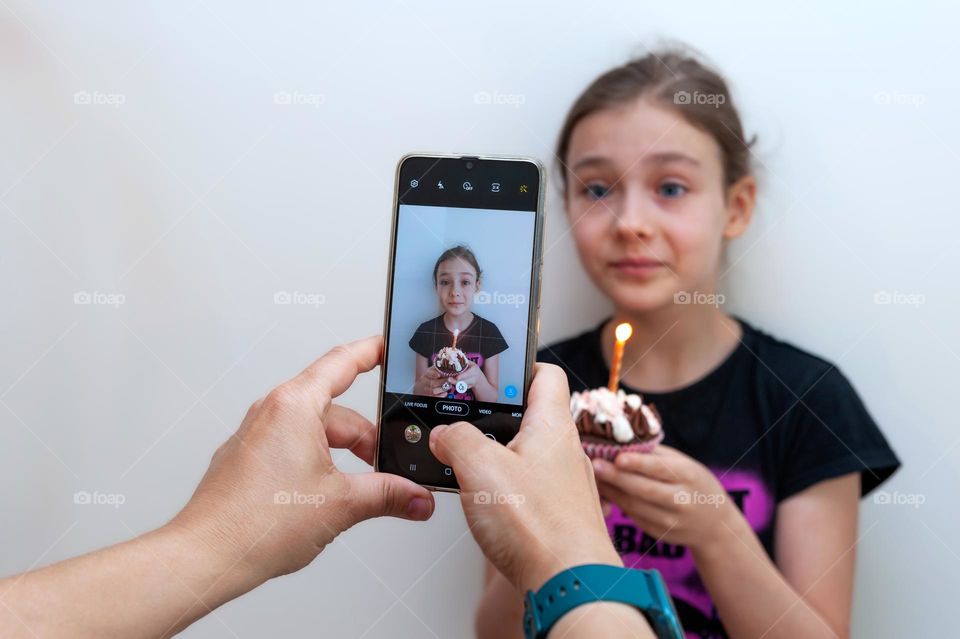 Make a wish. Picture of girl holding cupcake with candle taken with mobile phone.
