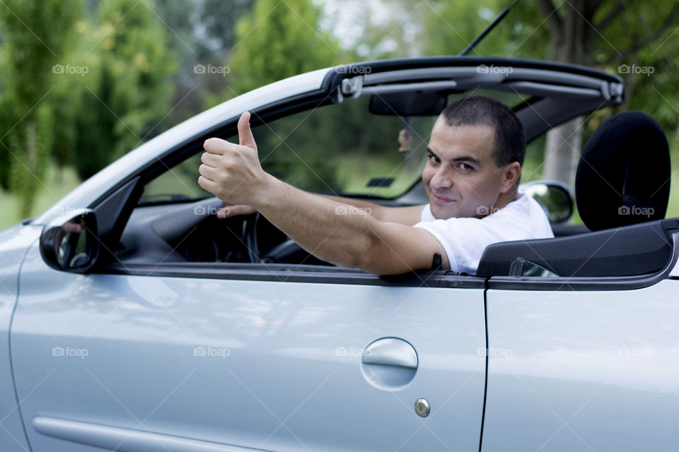 man giving thumbs up from car. attractive young man giving thumbs up from car and smiling,the car is convertible.