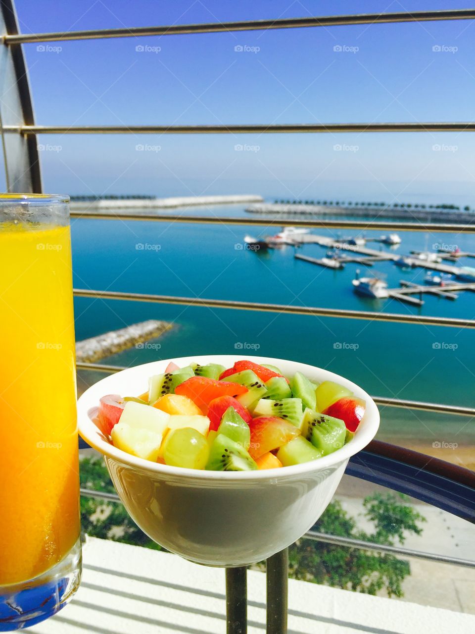 Fruit bowl and orange juice healthy breakfast overlooking the Oman harbour boats and sea 