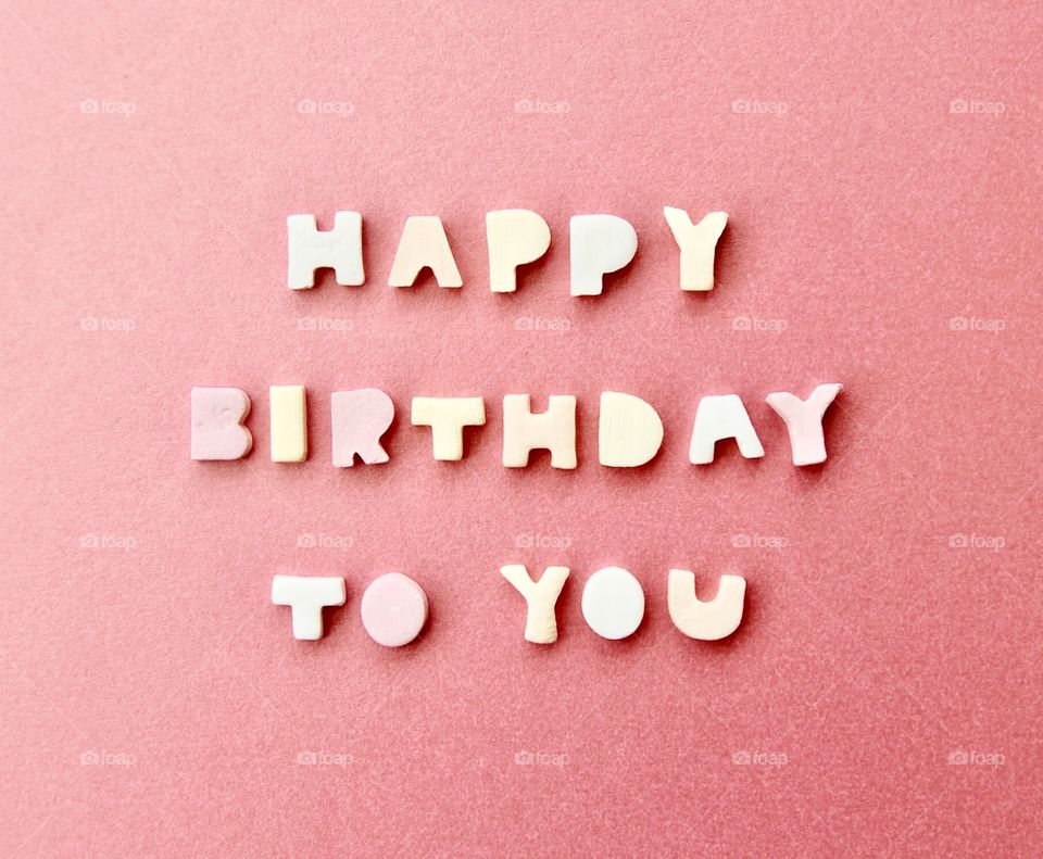 Happy birthday to you! A message spelled out using candy letters on a pink background. 