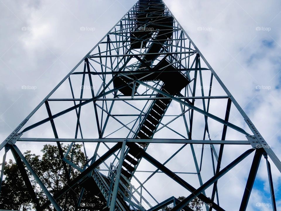 Low angle view looking up at fire tower. The steel beams result in geometric patterns against a cloudy sky.