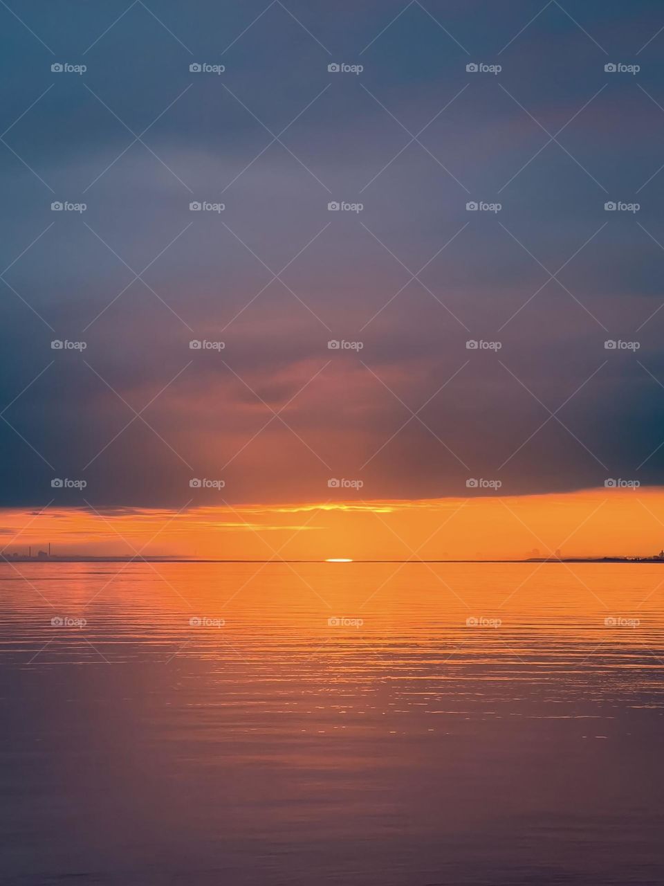 Beautiful colorful sunset reflecting in a lake, with the last sliver of the sun just about to dip below the horizon 