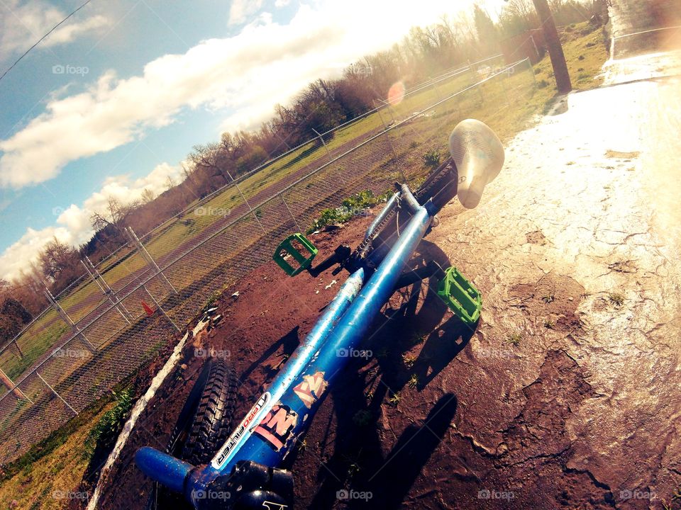 Blue bike with green pedals lays on it's side, under the sun, on a wet BMX race track.