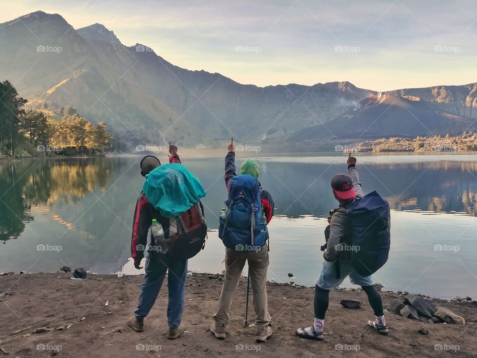 three backpackers stand at tge lake in the sunshine morning.